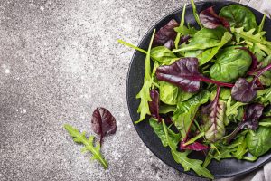 Um prato de saladas verdes em cima de uma mesa cinza.